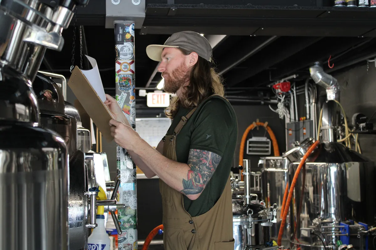 Tattooed Ceremony brewer checking the stainless fermentation tanks in the brewhouse