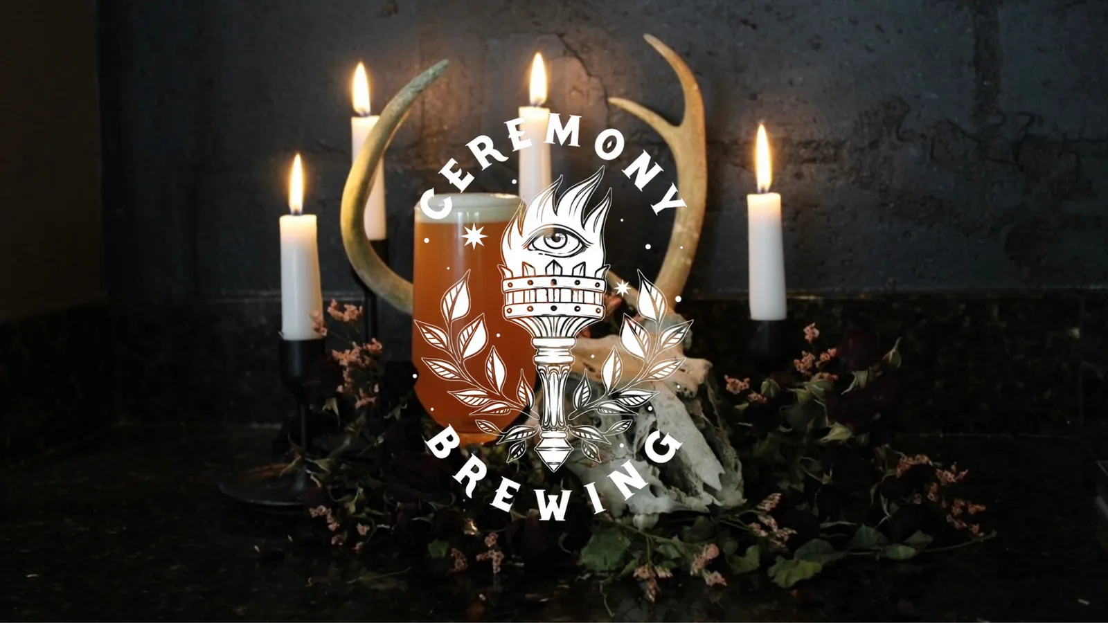 Candlelit Ceremony Brewing altar with antlers, a fresh pour and the torch-and-eye logo